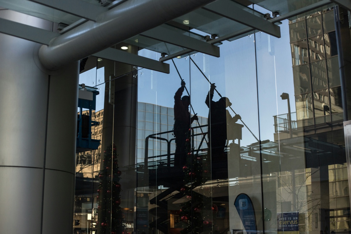 A Groupe Impec technician cleaning a glass façade at height, on ropes
